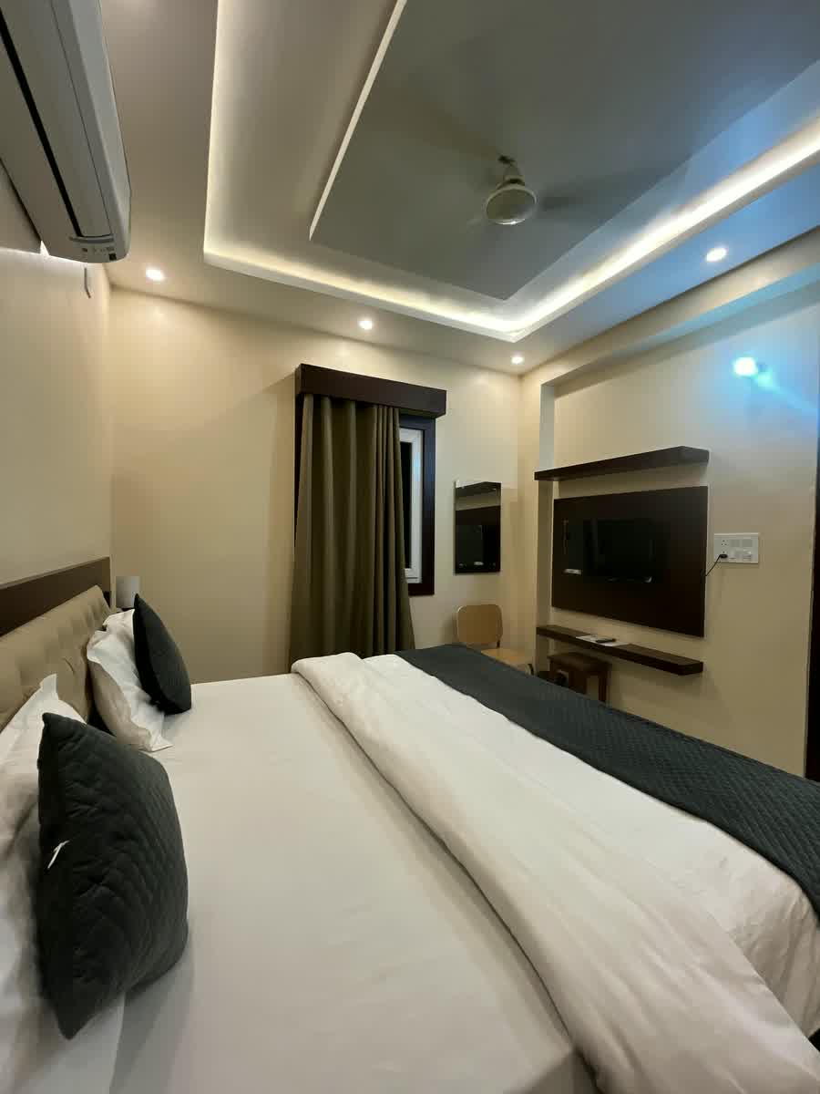 Close by the bed: white linen, dark cushions and the television unit beyond.